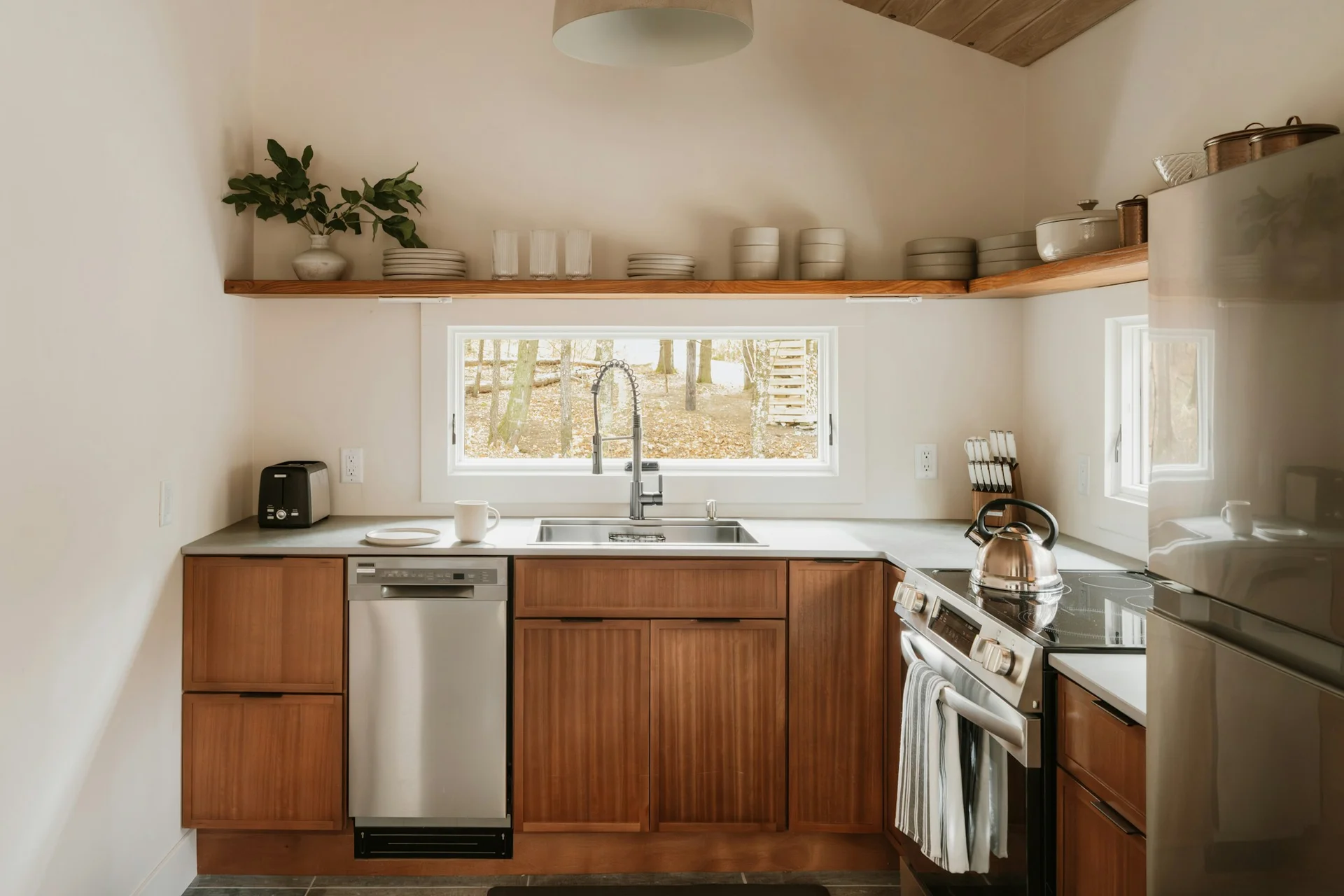 Cuisine compacte en bois avec étagères ouvertes et fenêtre donnant sur les arbres.